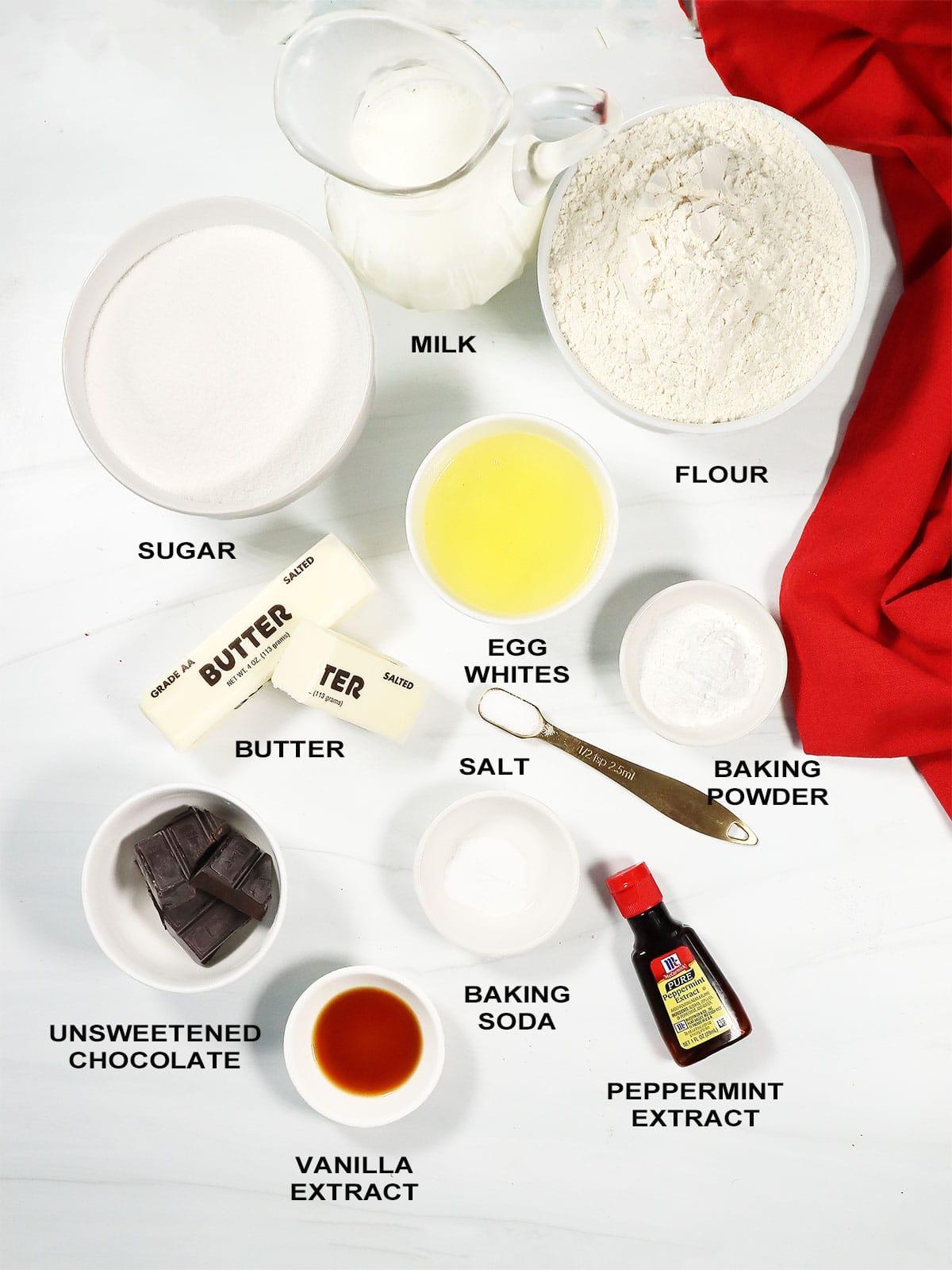 Various baking ingredients including cocoa powder, peppermint extract, butter, and sugar laid out on a marble counter