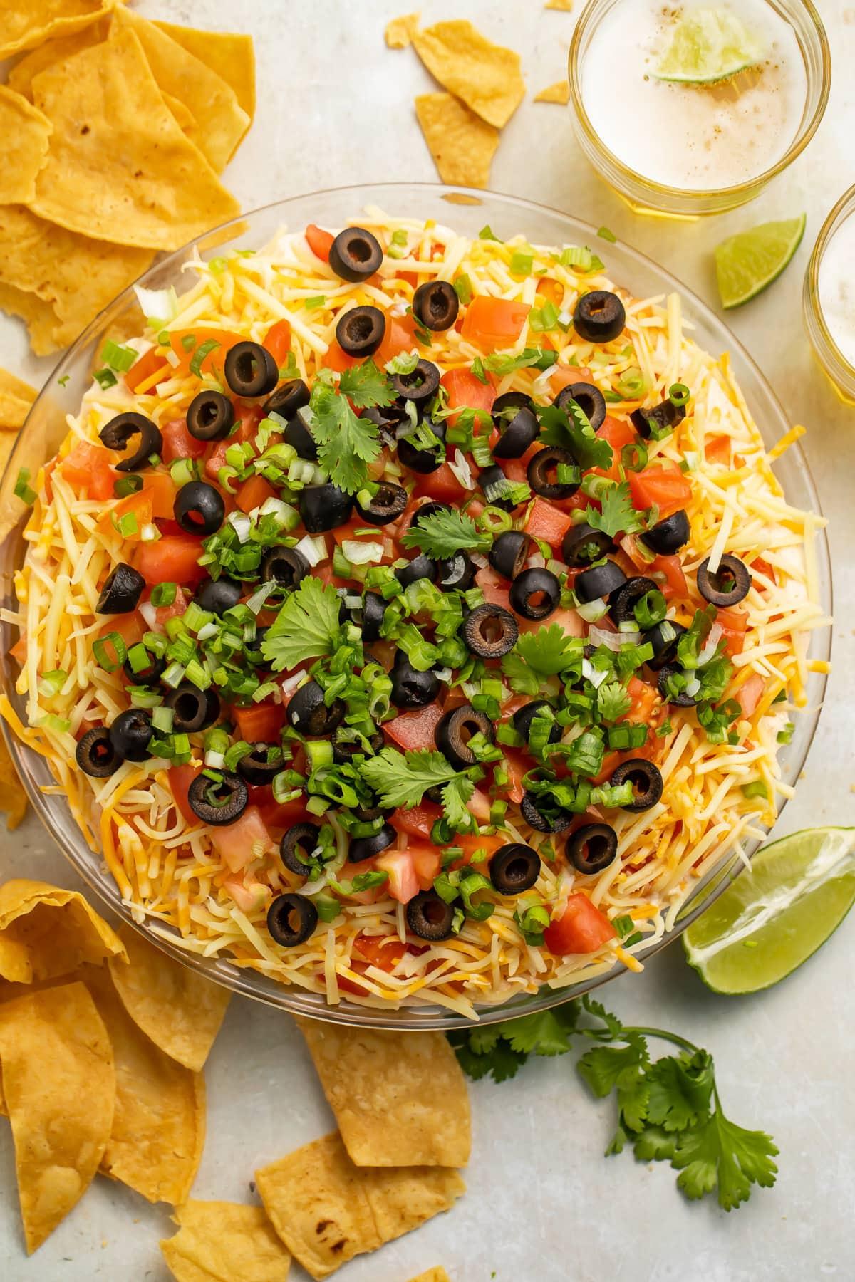 A visually appealing seven layer dip with baked tortilla chips, garnished with cilantro and sour cream.