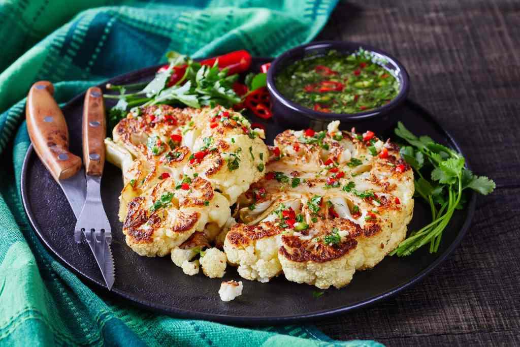 closeup of perfectly seared cauliflower steaks with vibrant radishes and fresh herbs