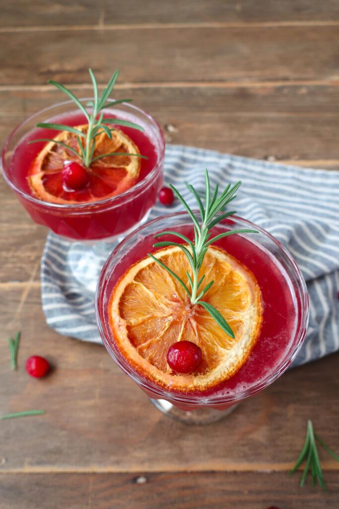 Ingredients laid out for cranberry spritz: fresh cranberries, oranges, rosemary, cranberry juice, sparkling water, sugar