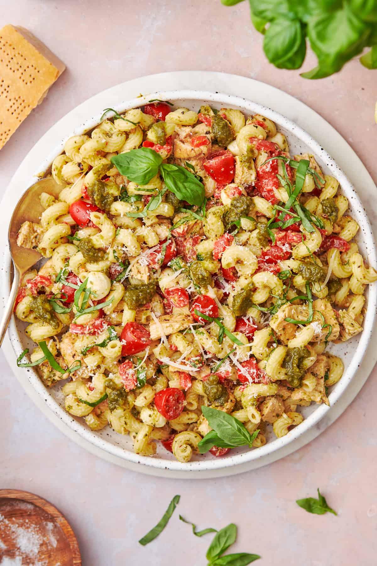 Close-up shot of Pesto Chicken Pasta Salad with visible basil leaves and cheese crumbles.