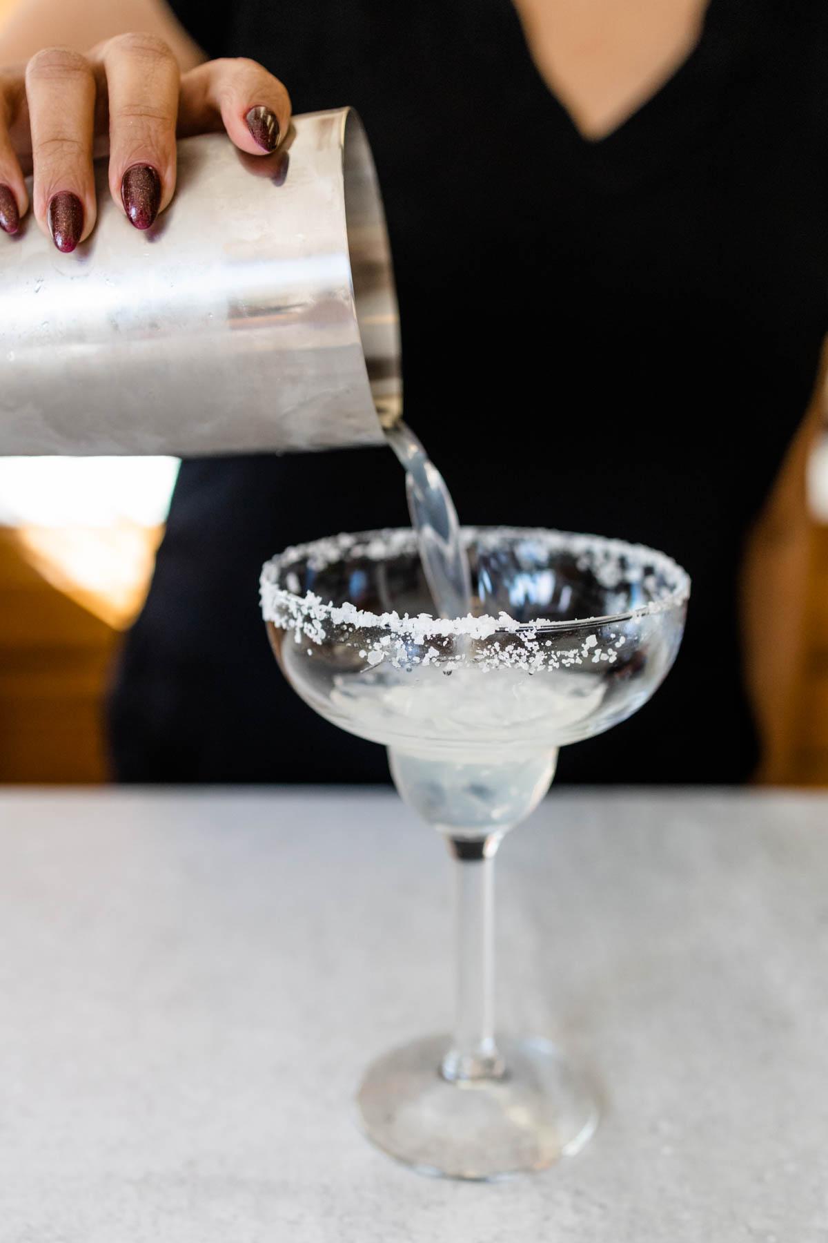 pouring basil margarita into a salted rim glass
