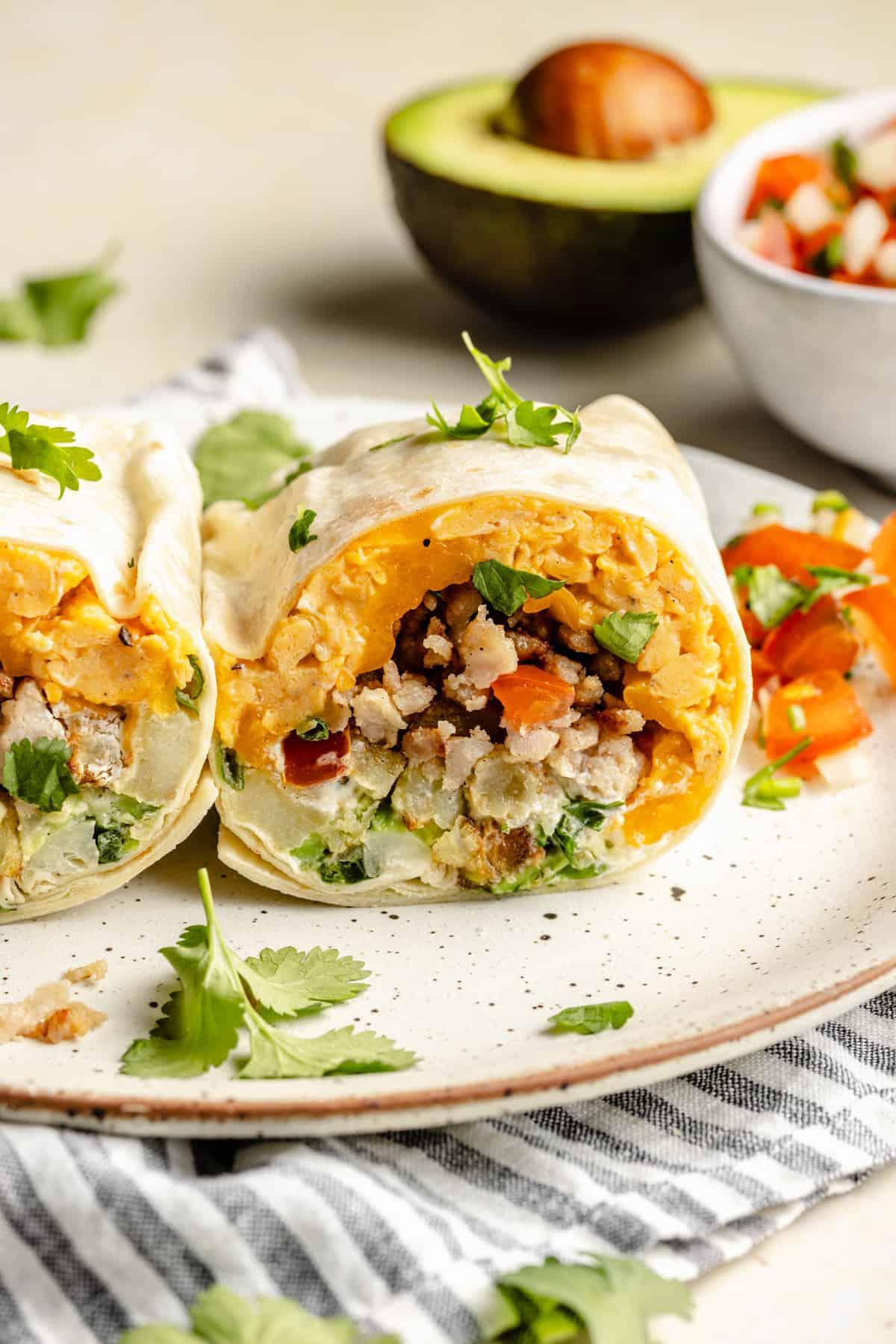 Close-up of hands assembling a breakfast burrito with visible ingredients: scrambled eggs, sausage, salsa, cheese