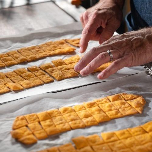 Golden sharp cheddar cheese crackers cooling on a wire rack, with some broken pieces revealing a flaky texture.