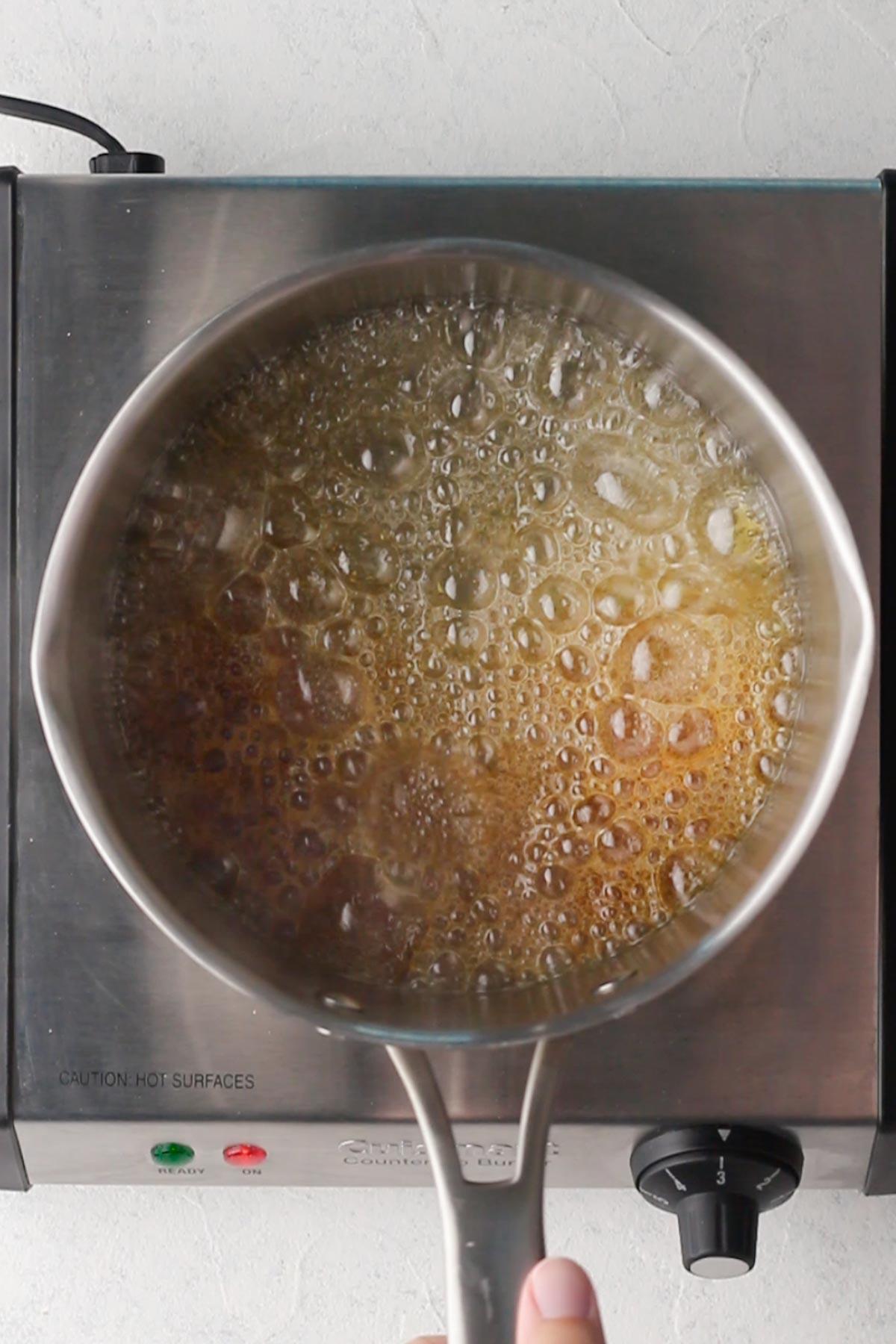 Someone stirring a batch of homemade salted caramel sauce in a saucepan