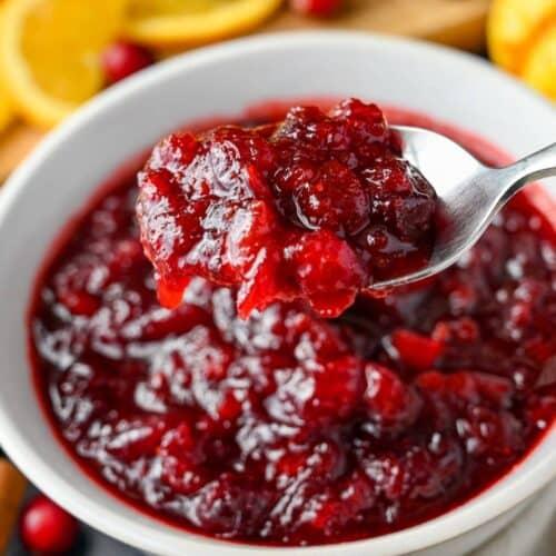 Homemade slow-simmered cranberry sauce with whole cranberries and orange zest in a rustic bowl, close up, warm lighting