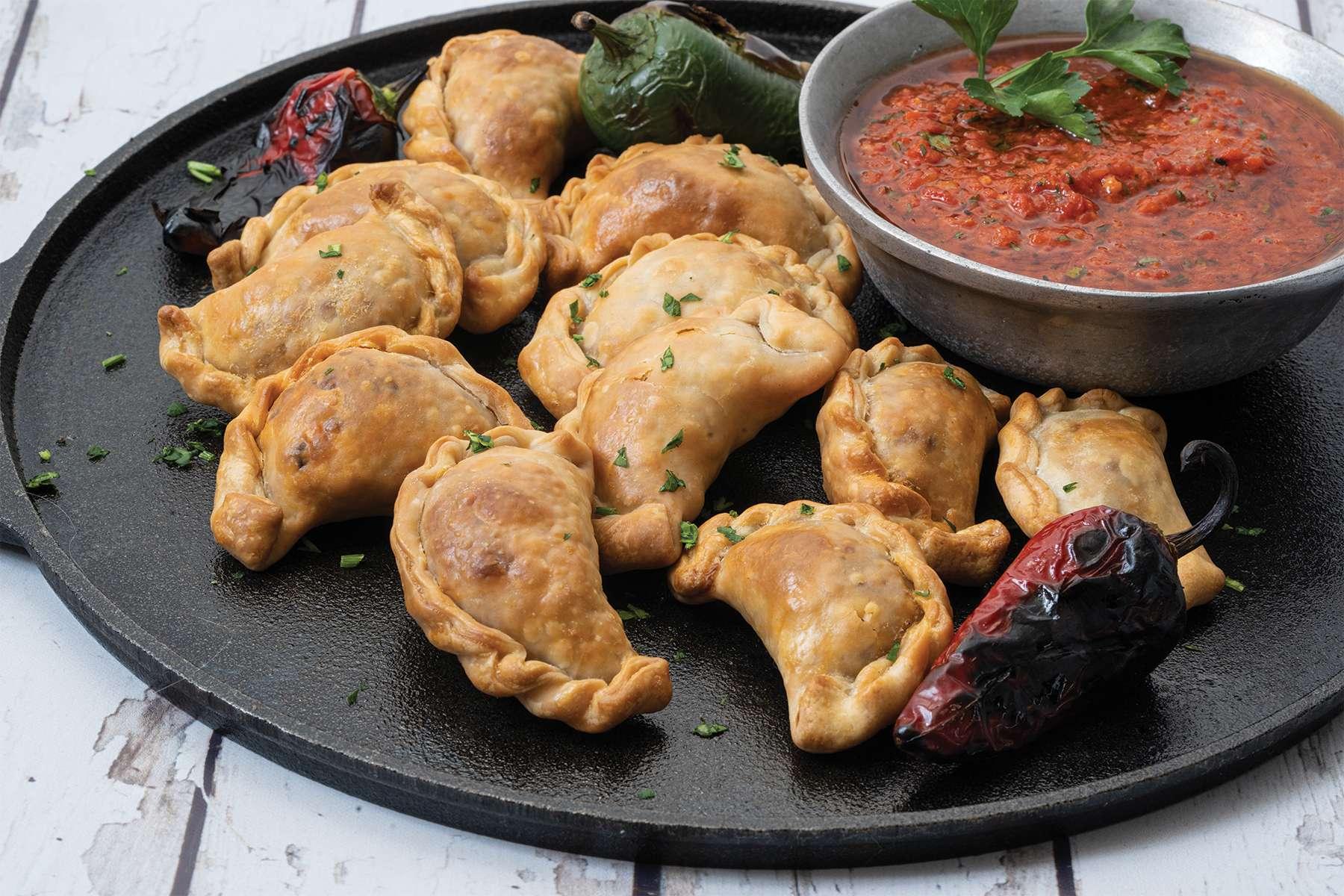 Golden brown Easter lamb empanadas arranged on a rustic wooden board, garnished with fresh chimichurri sauce