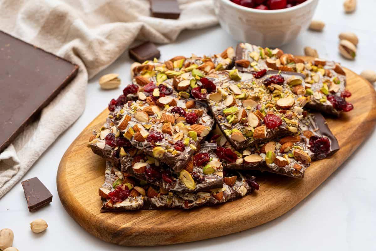 Ingredients for chocolate bark on a wooden cutting board, various chocolates, nuts, dried fruit