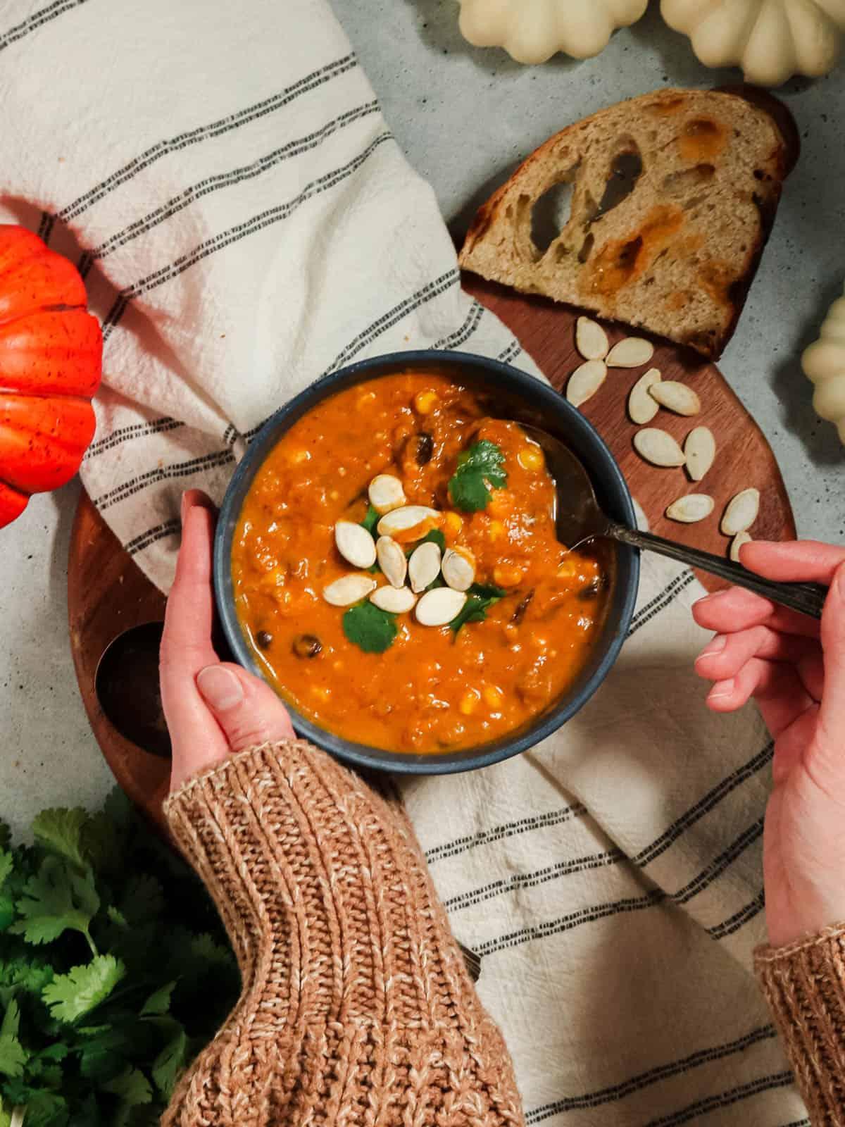 overhead shot of someone stirring a pot of pumpkin soup with herbs