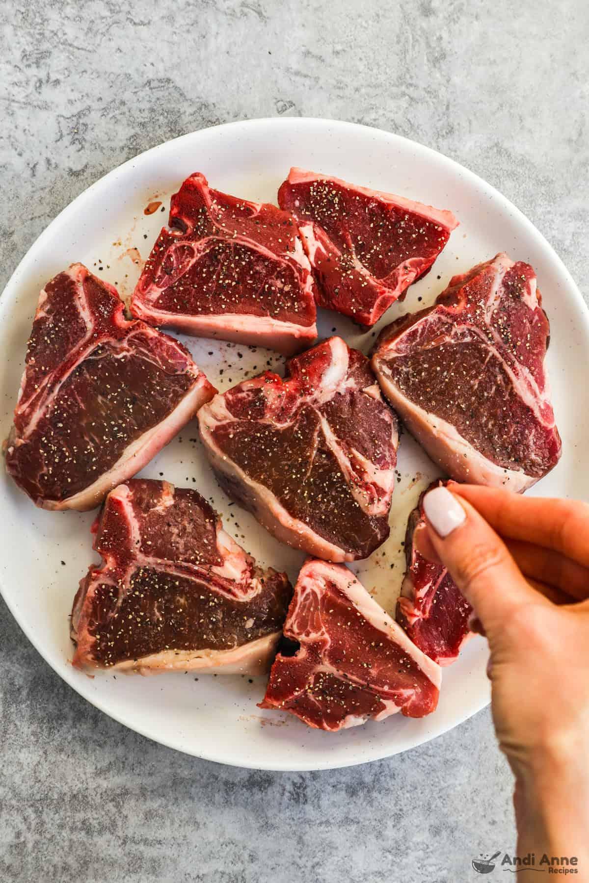 raw lamb chops being seasoned with salt and pepper