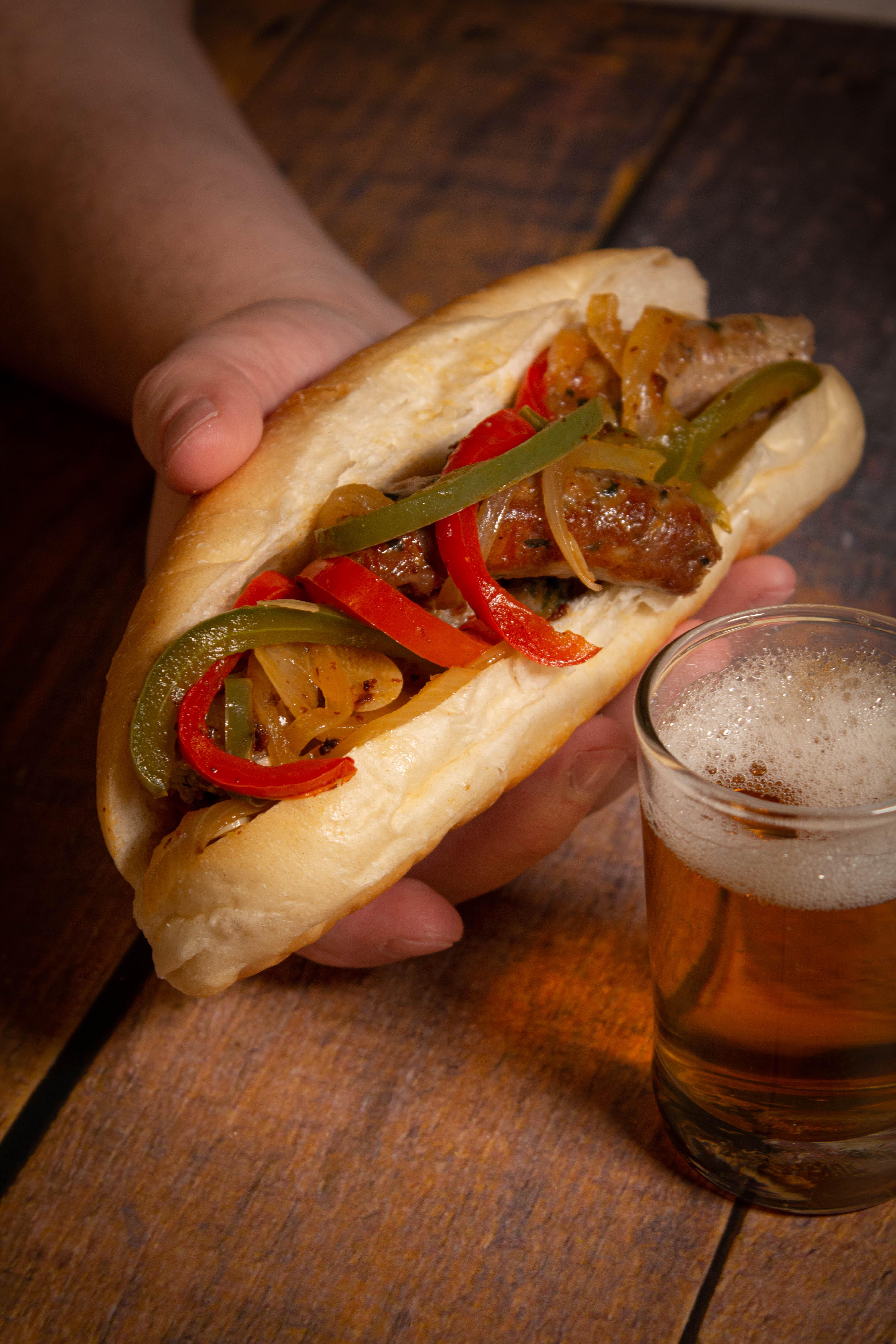 close up of a hand holding a sausage and pepper hoagie