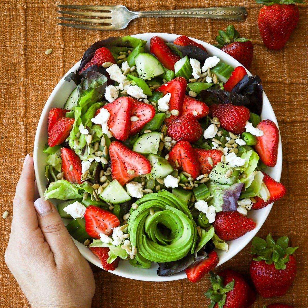 close-up of fresh strawberries and leafy greens being prepared for the salad