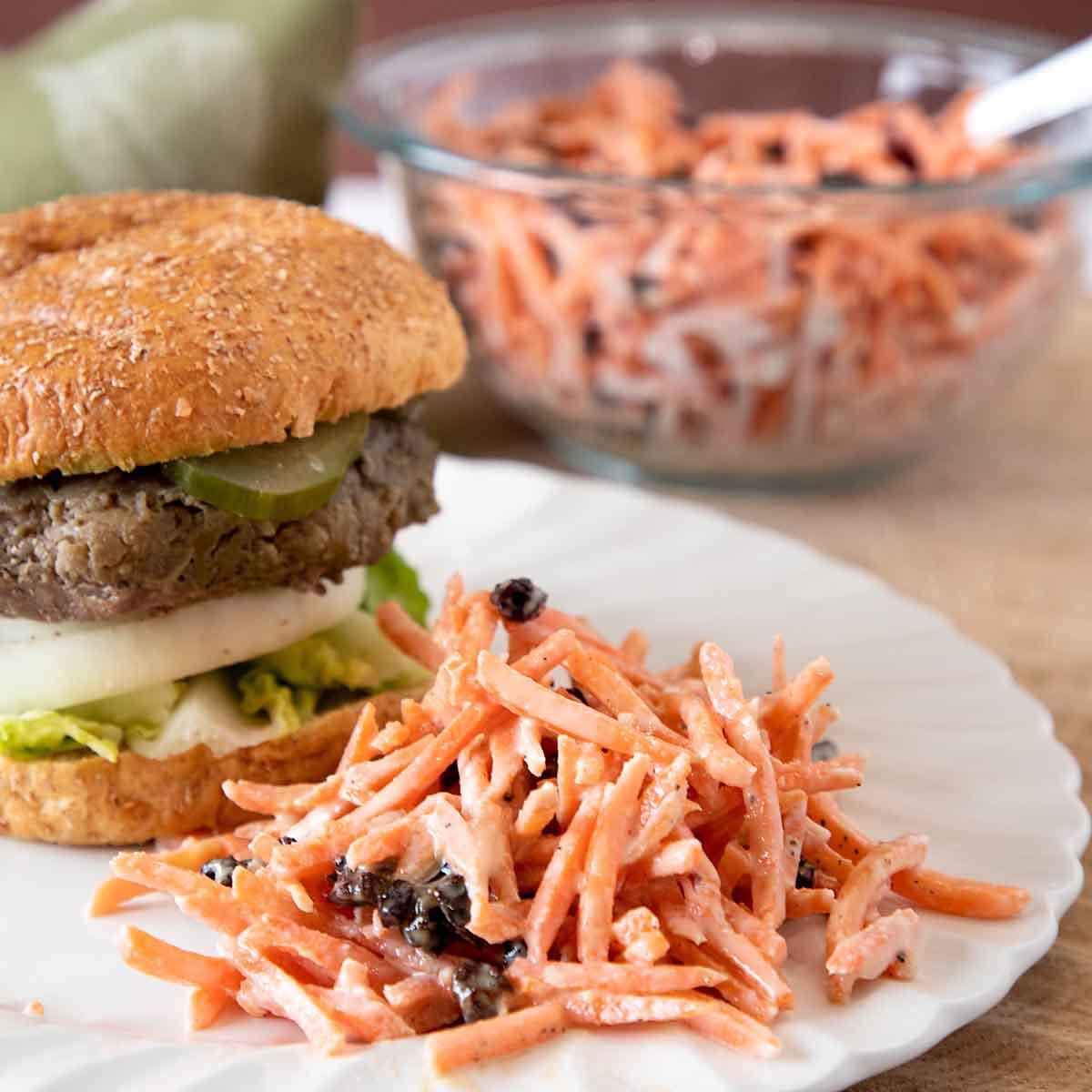 a bright and airy shot of a carrot and raisin salad served on a plate with a sandwich, showcasing it as a side dish