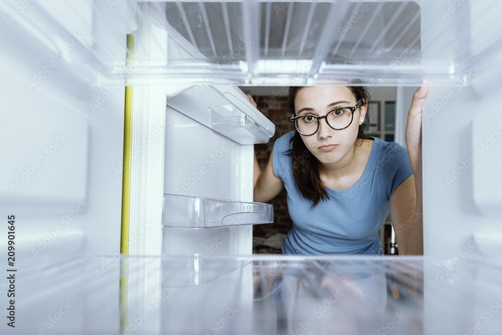Woman looking tiredly into an empty fridge on a busy weeknight