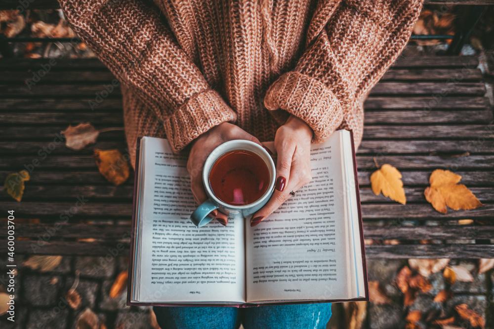 Close-up of a hand holding a steaming mug of hot chocolate, a cozy book in the background