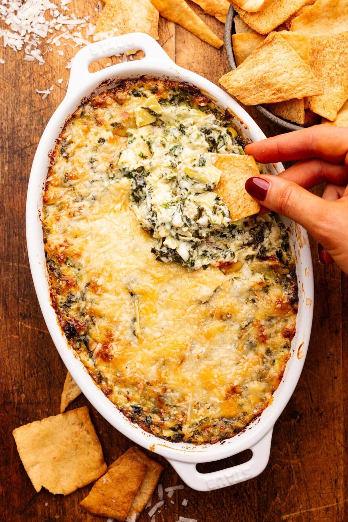 overhead shot of baked spinach artichoke dip in a rustic serving dish with dippers around