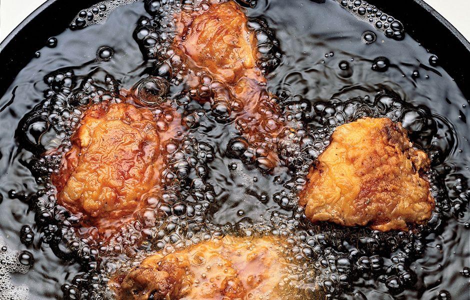 Close-up shot of hands frying chicken in a cast iron skillet