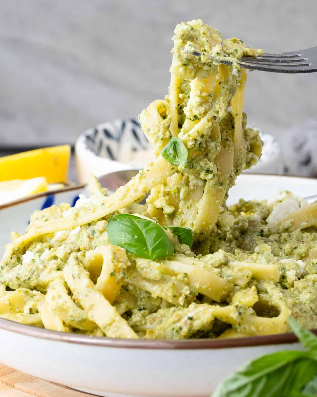 Close-up of hands tossing gluten-free pasta with vibrant pesto.