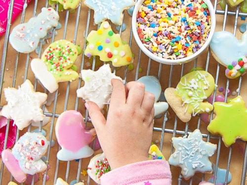 Child excitedly decorating a sprinkle sugar cookie with colorful sprinkles and smooth icing
