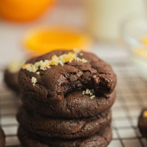 stack of glossy chocolate orange cookies on a rustic wooden board with a cup of coffee