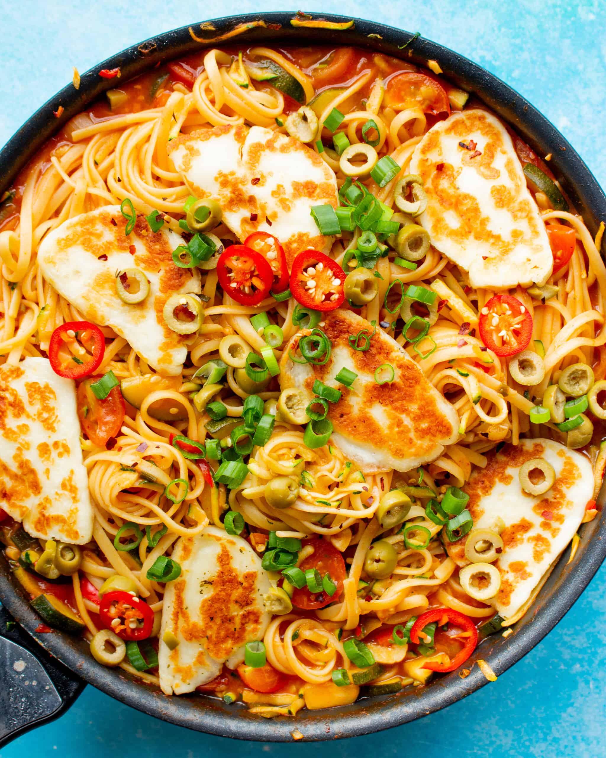 A close-up shot of a perfectly grilled halloumi slice next to a pile of cooked ramen noodles, and a small bowl of vibrant green mint chutney