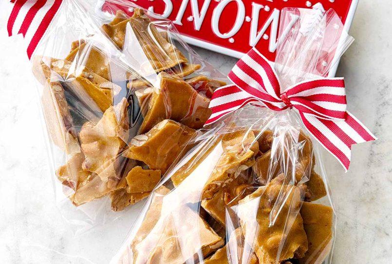 An array of beautifully wrapped homemade peanut brittle pieces, tied with festive ribbons, ready for gifting.