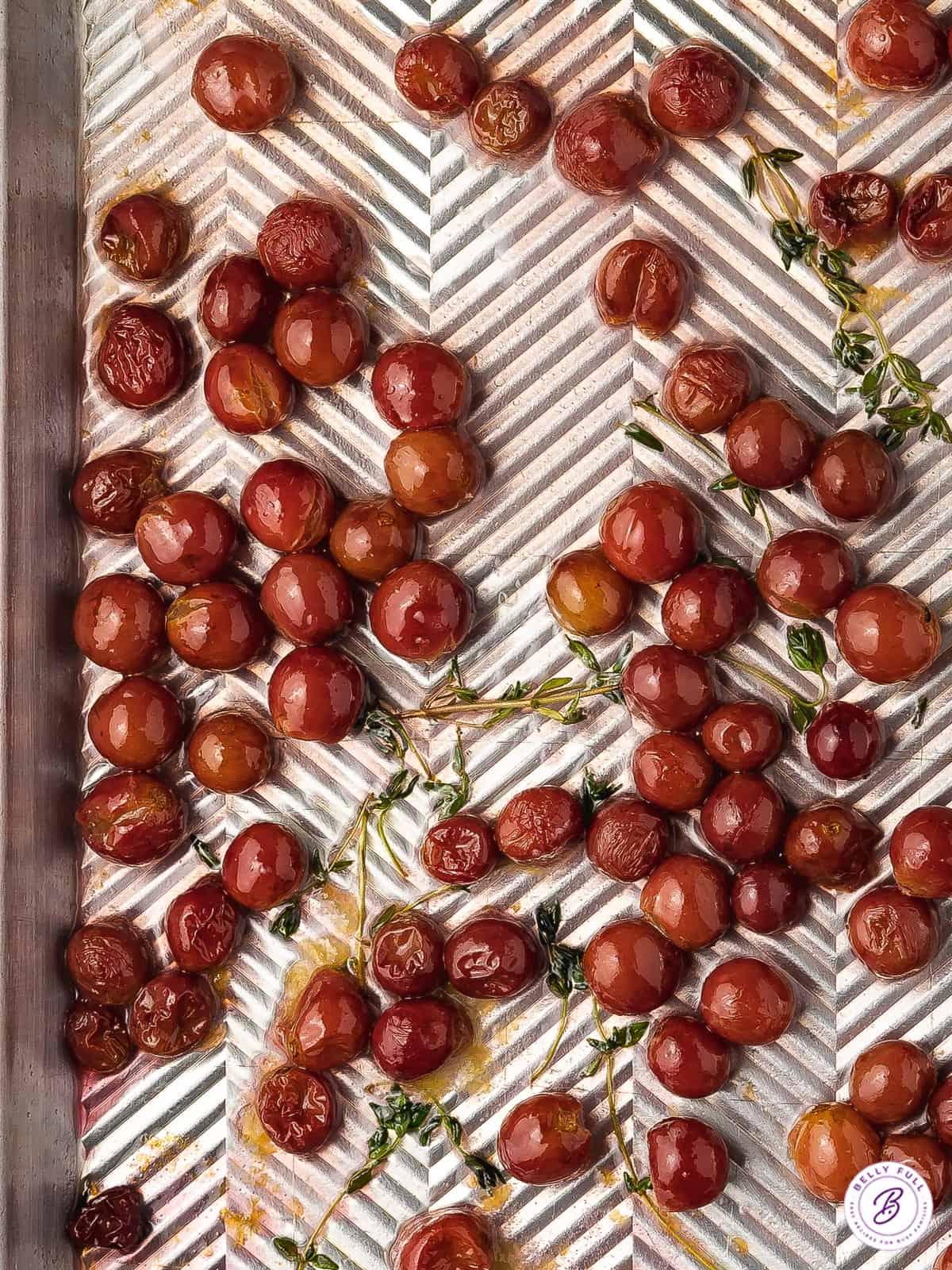 Vibrant roasted red grapes on a baking sheet with fresh thyme and olive oil