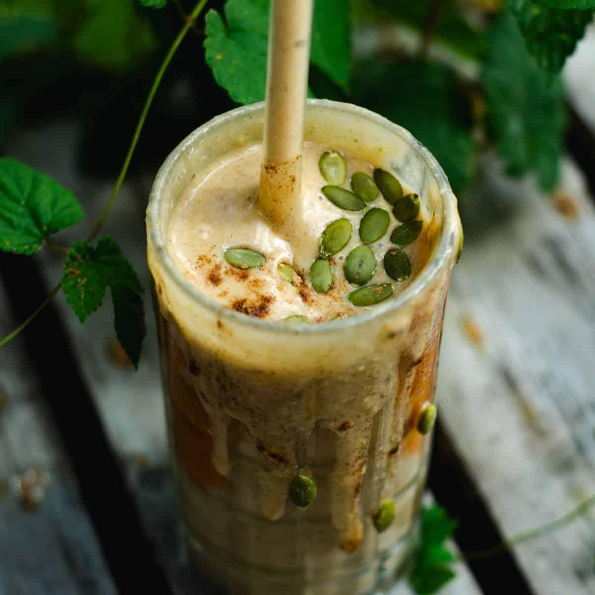 Pumpkin seed almond energy smoothie in a glass with ingredients around it