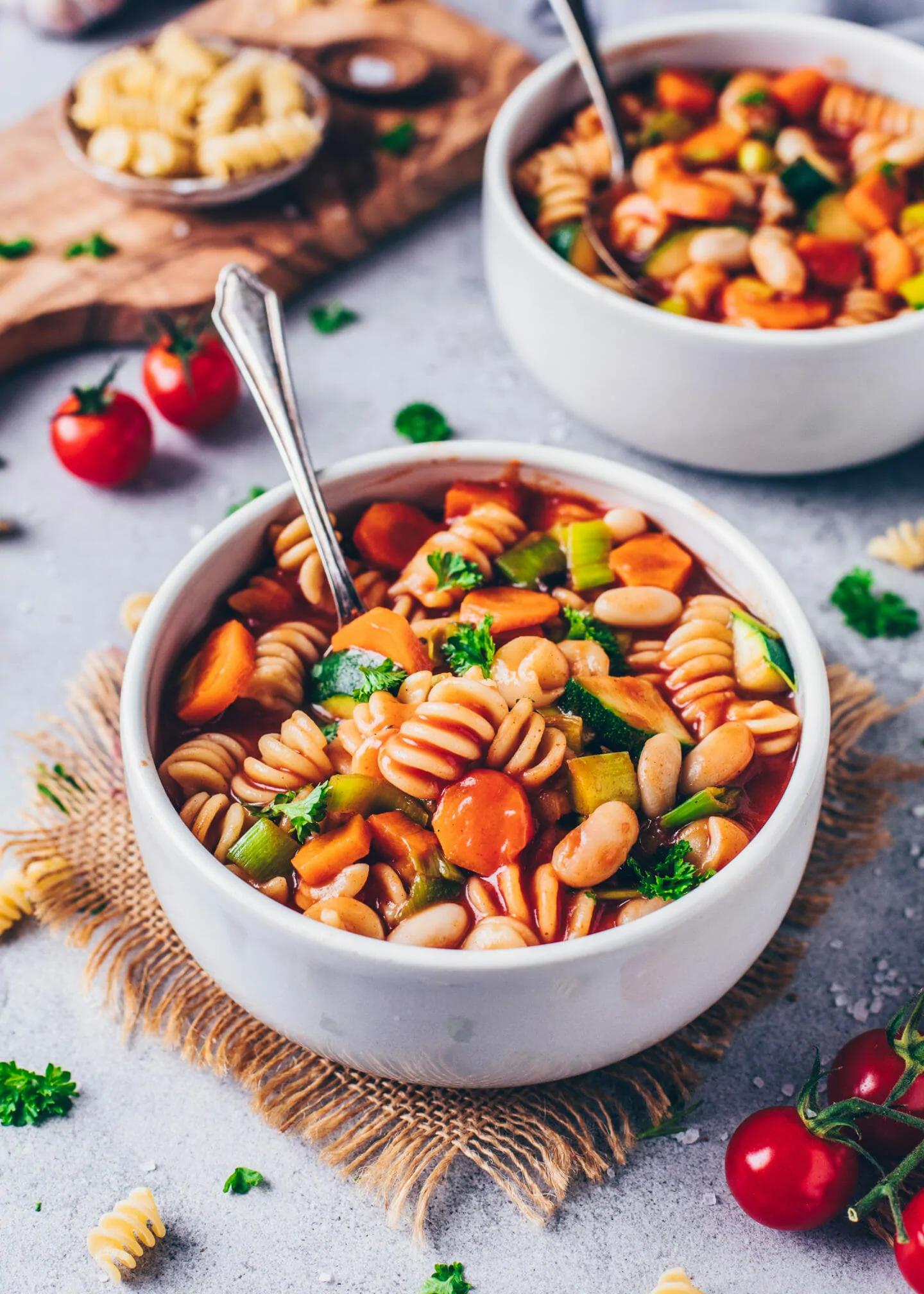 Close-up of a bowl of vegan minestrone soup garnished with vegan cheese and fresh herbs