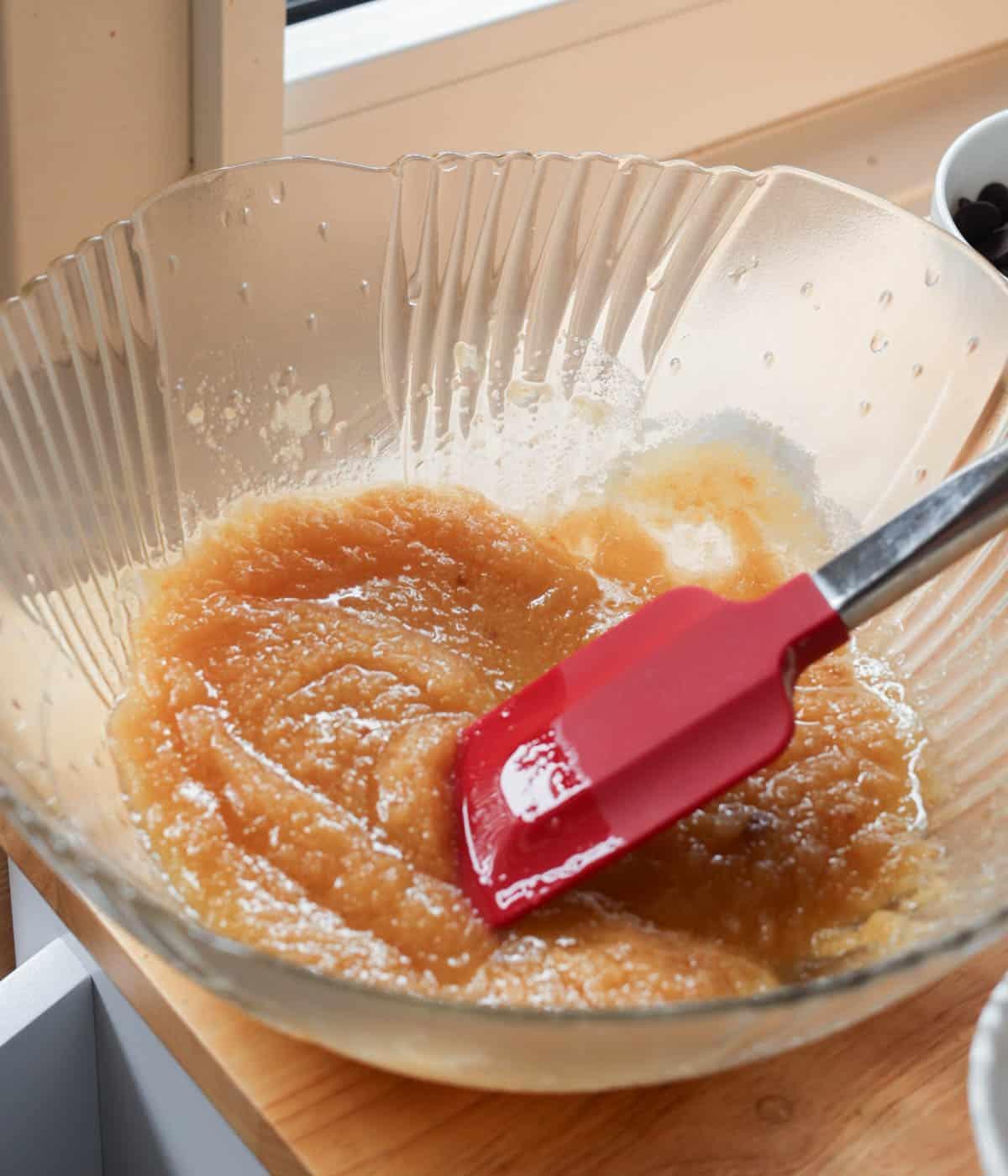 Close-up of banana walnut bread batter being mixed gently in a glass bowl with a rubber spatula