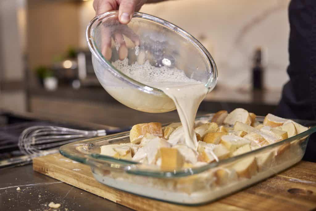 a baker pouring custard over a pan of stale bread cubes