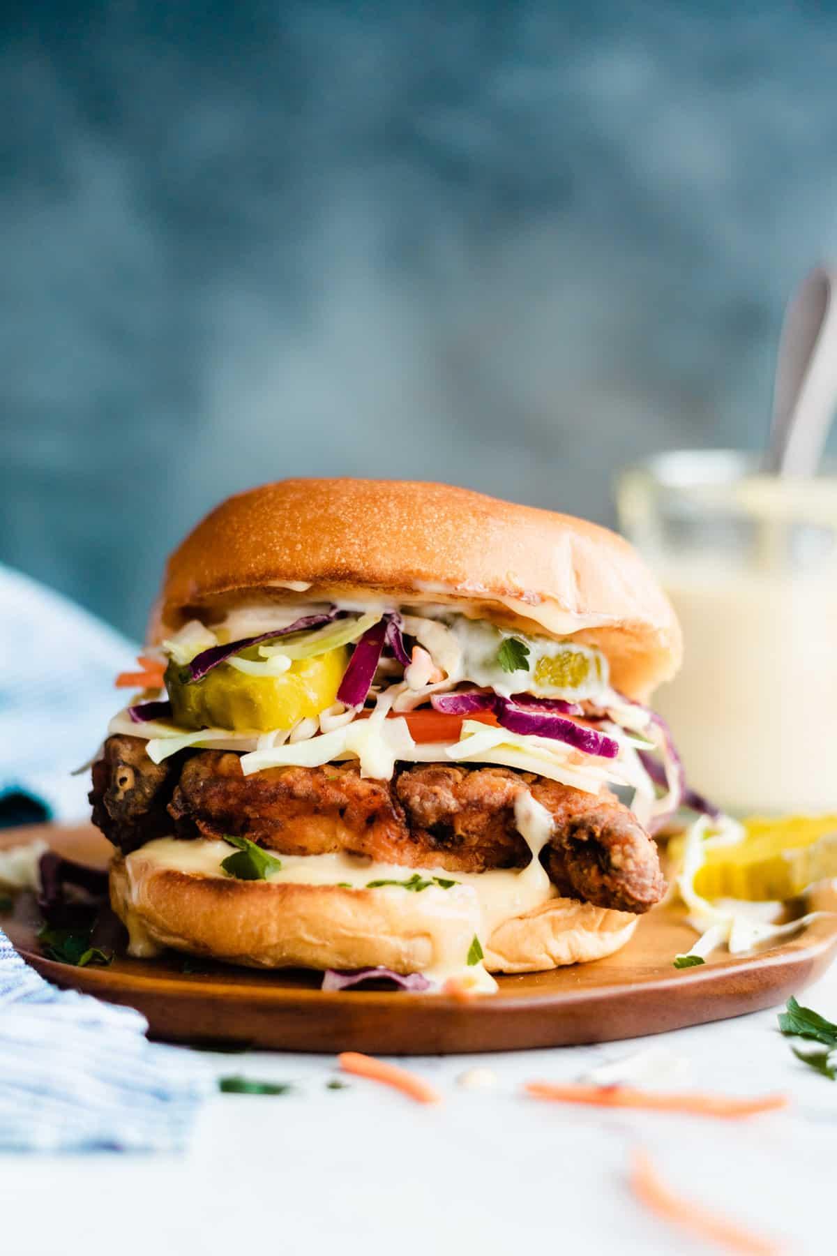 a hand holding up a fried chicken bagel sandwich with honey mustard dripping down the sides