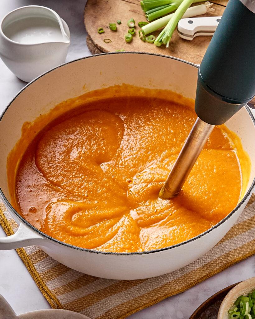 A hand dipping a carrot stick into smoked paprika and sweet potato miso