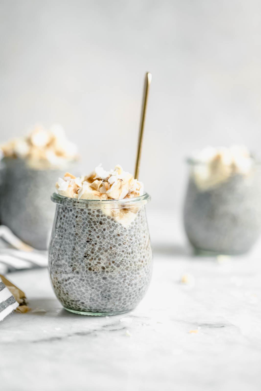 A close-up shot of a creamy, light-brown chia pudding layered with toasted coconut flakes and a lime wedge