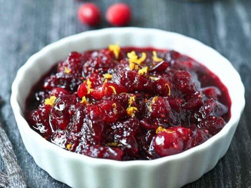 Vibrant homemade cranberry sauce with a vanilla bean pod and fresh cranberries in a rustic ceramic bowl, set on a festive holiday table.