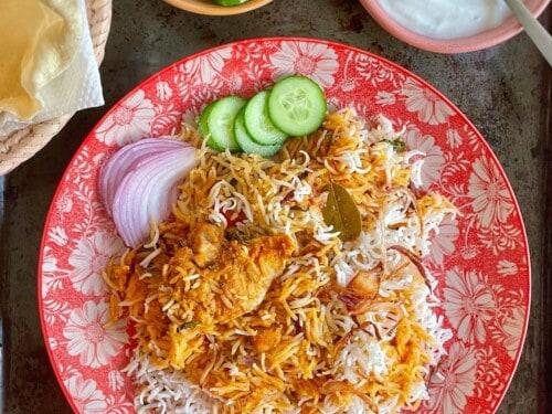 A person preparing Chicken Tikka Biryani, focusing on the layering process