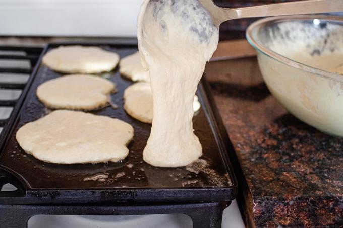 close-up of a hand pouring pancake batter onto a hot griddle