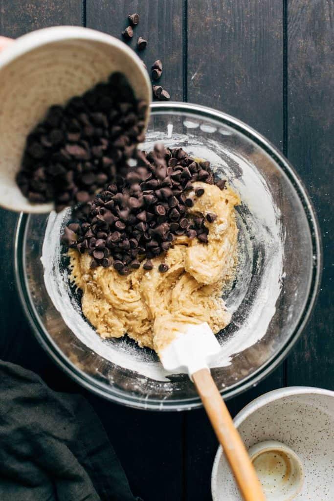 Hands gently folding chocolate chips into cookie dough in a mixing bowl