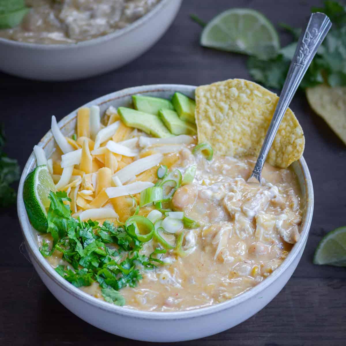 Creamy white chicken chili topped with avocado, cilantro, and tortilla strips in a rustic bowl on a wooden table, cozy setting