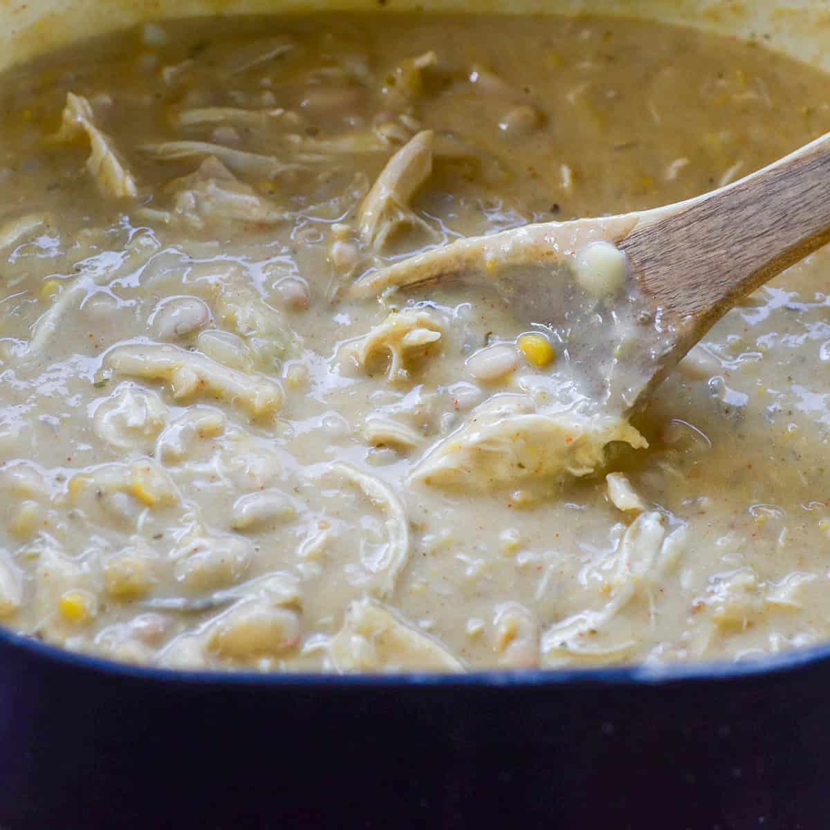 close-up of white chicken chili simmering in a large pot on the stove, steam rising, with a wooden spoon stirring it