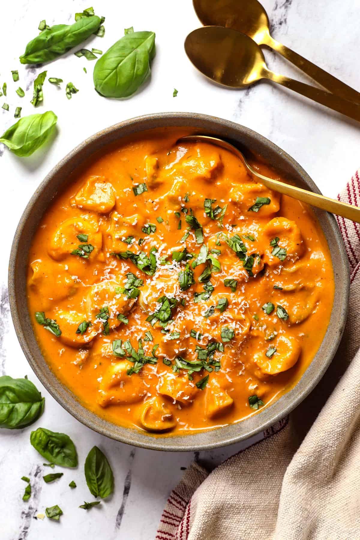 a steaming bowl of tomato tortellini soup, garnished with pesto and parmesan cheese