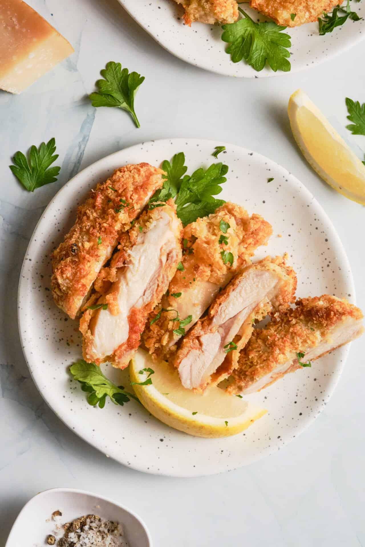 Crispy golden parmesan chicken cutlets on a plate with fresh parsley garnish and lemon wedges