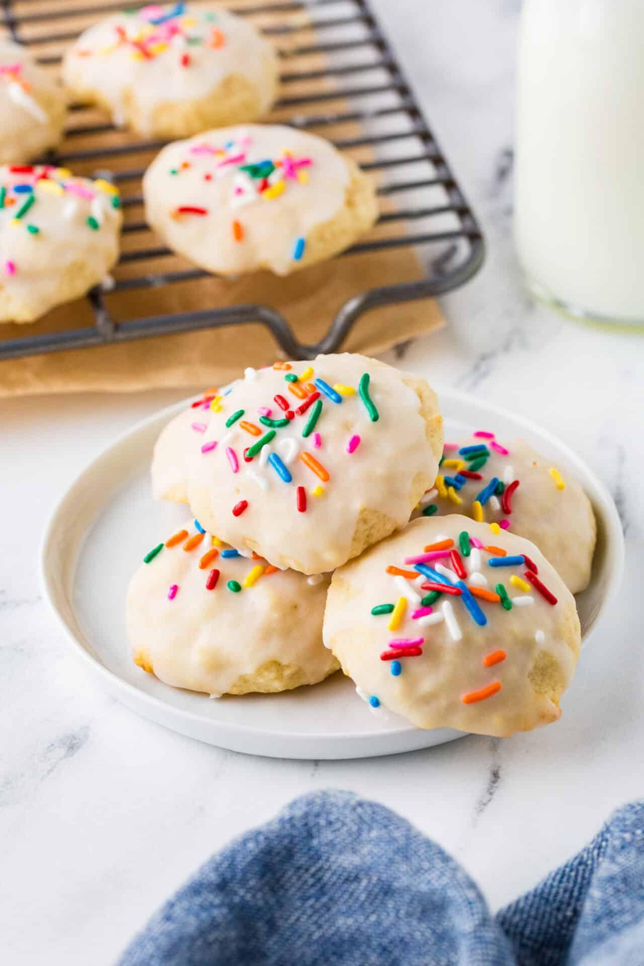 vibrant sprinkle sugar cookies with smooth vanilla icing on a white plate, cooling rack in background, natural light