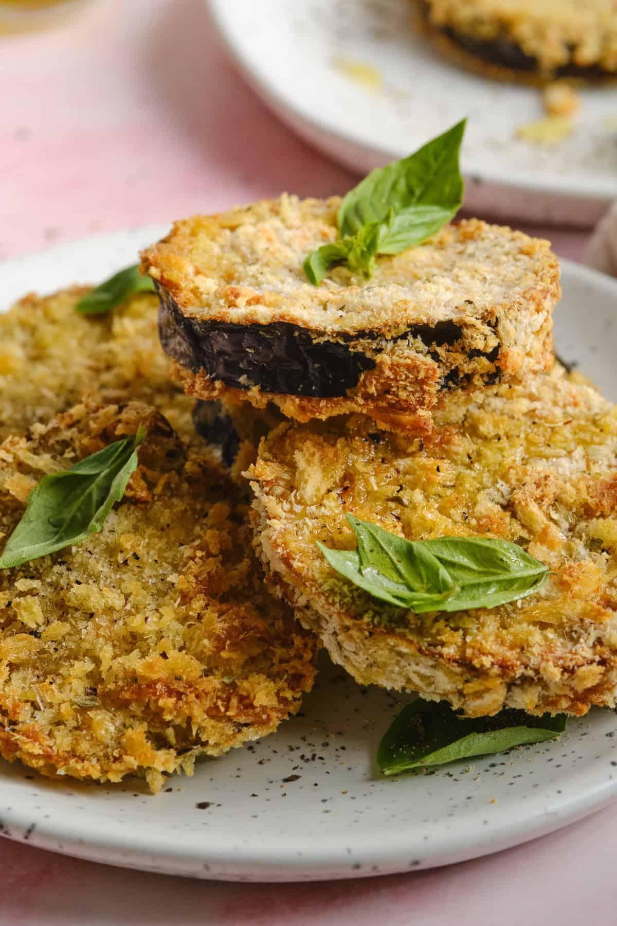 Crispy tempura-fried eggplant slices arranged artfully on a plate, drizzled with vibrant green pesto sauce
