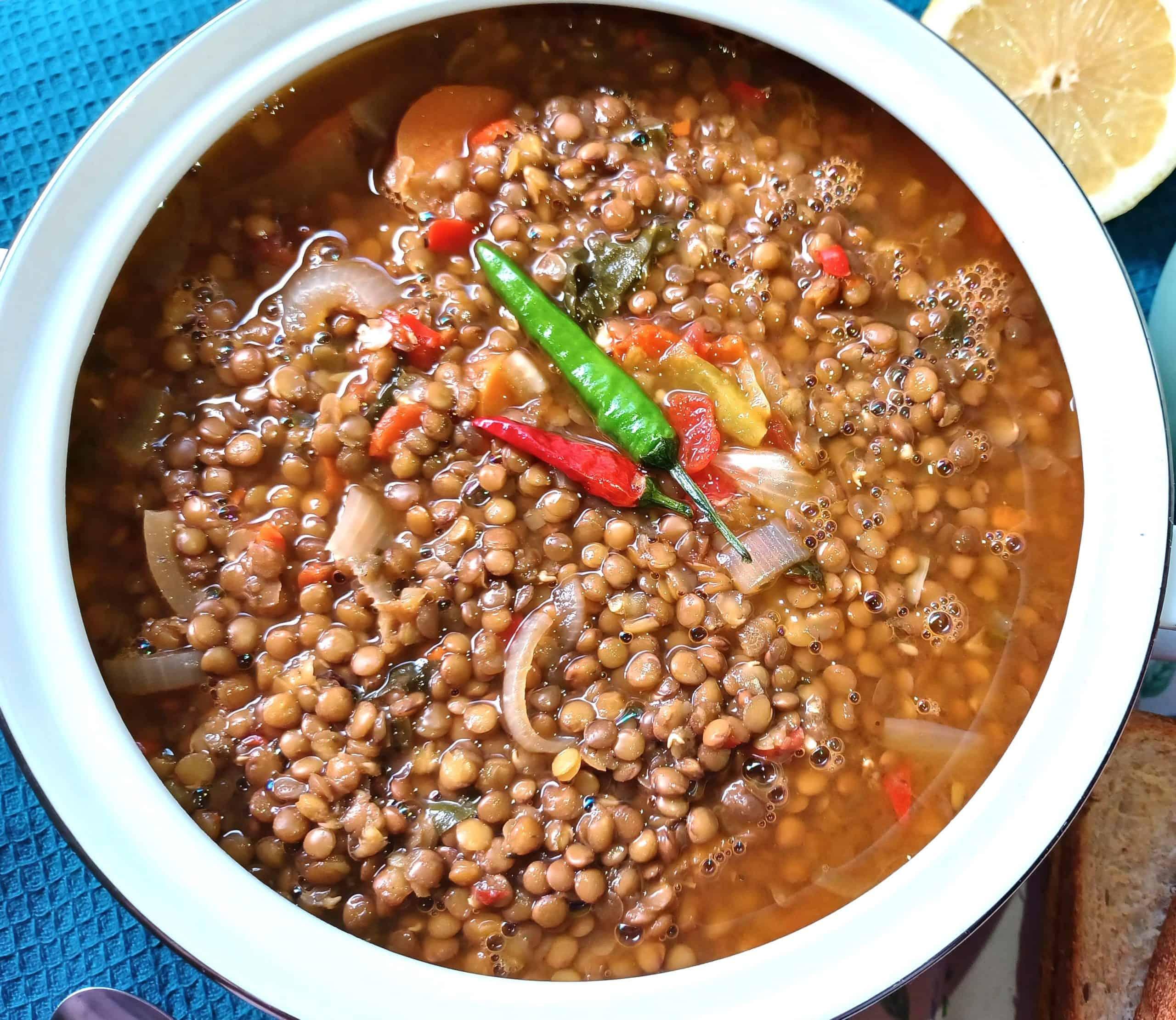 Close-up of a bowl of lentil soup with roasted garlic cloves and fresh thyme, steam rising