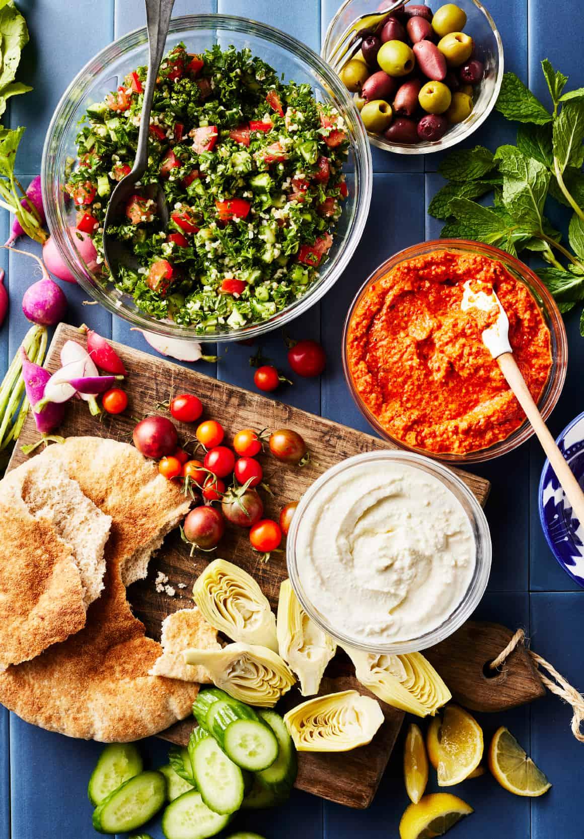 overhead shot of a table with currant tzatziki, pita bread, and assorted vegetables