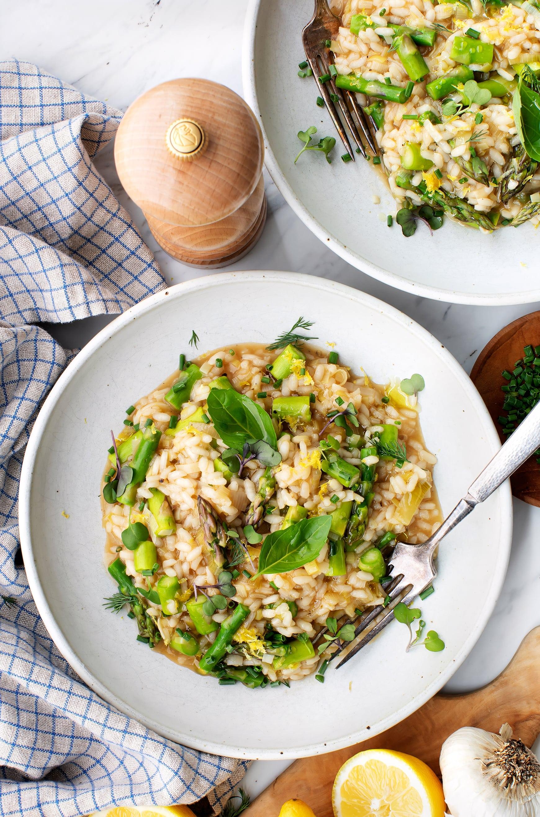 Asparagus risotto topped with a crispy parmesan cheese garnish, served in a rustic bowl on a wooden table with a glass of white wine