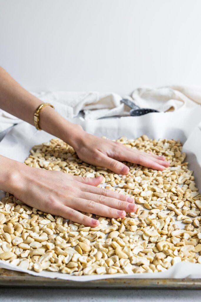 A person carefully spreading cashew mixture on a baking sheet