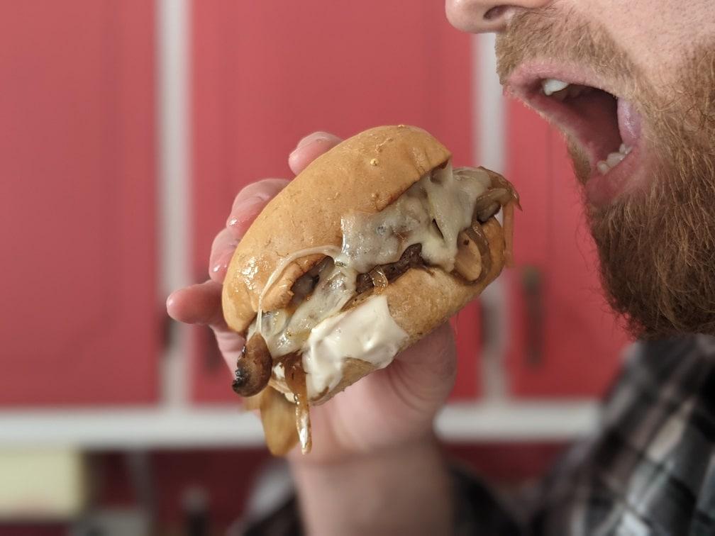 person taking a bite of the philly cheesesteak burger with provolone dripping