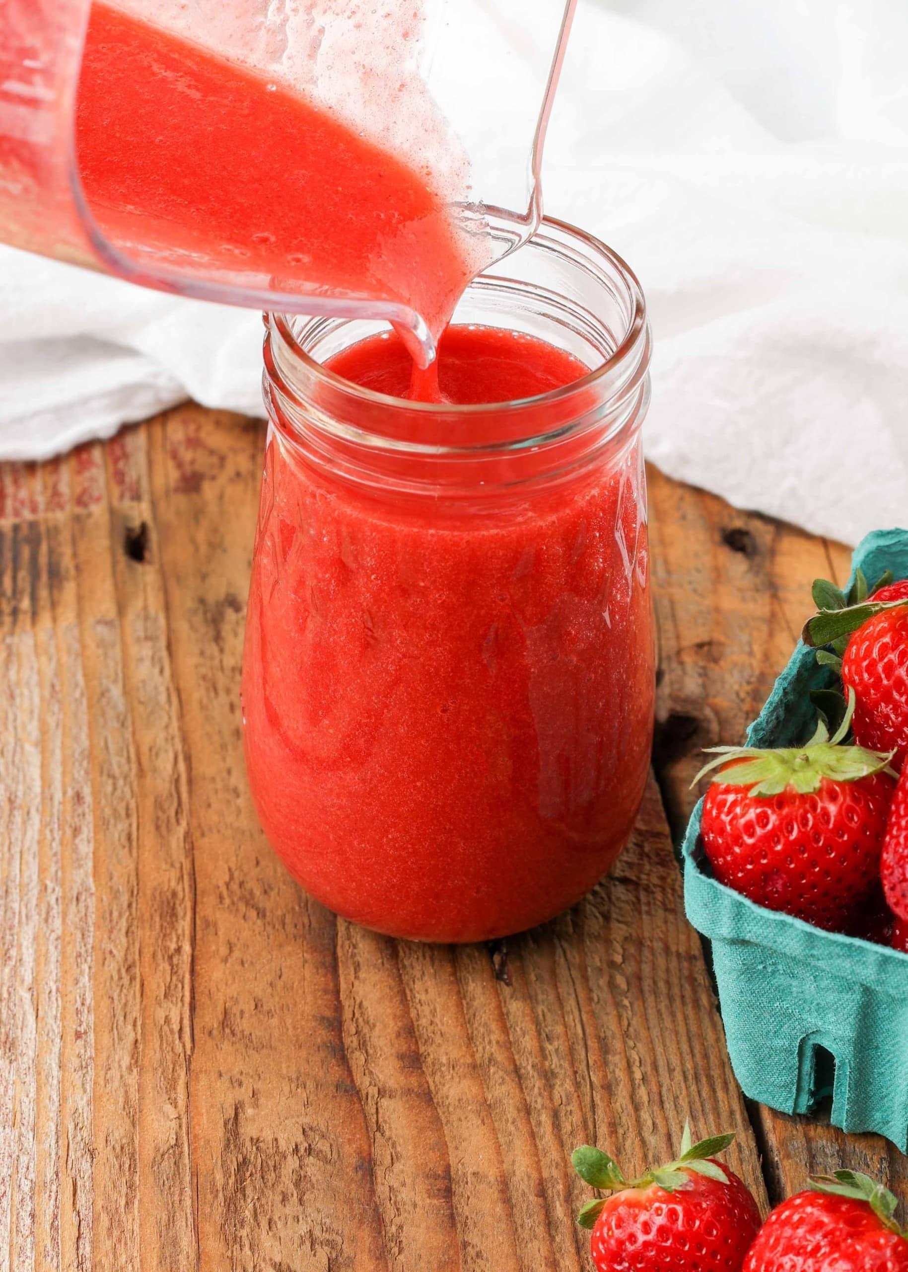 A close-up of a pitcher filled with bright red strawberry puree
